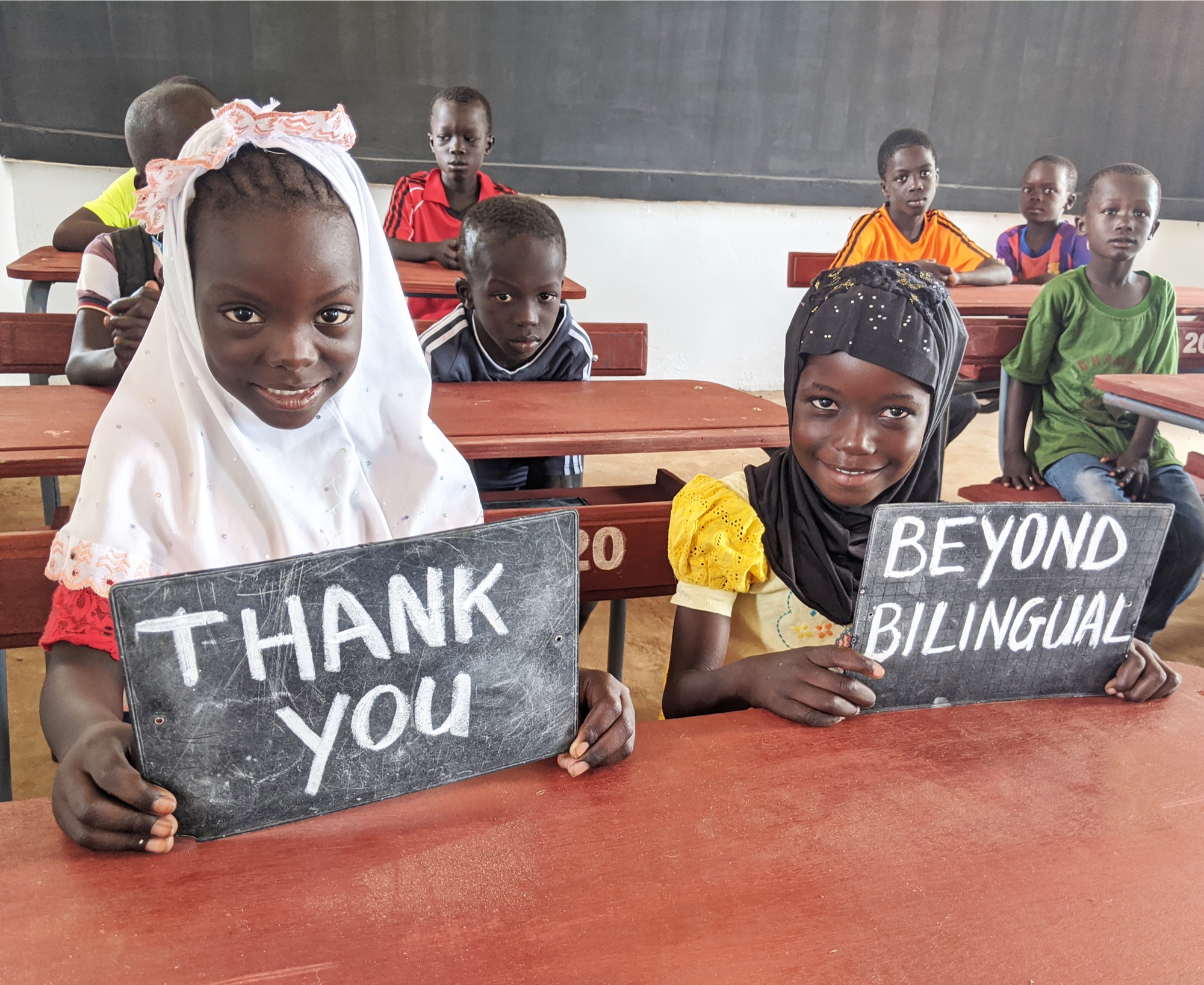 Impact Beyond Recruitment 5 Students seated at desks inside the completed Senegal school, holding thank-you signs